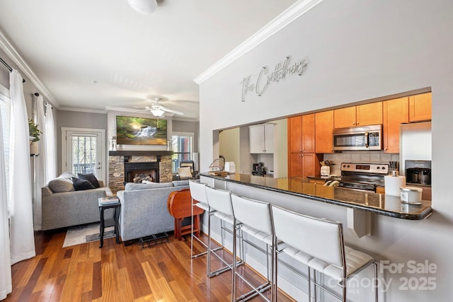 kitchen with a kitchen breakfast bar, dark countertops, ceiling fan, appliances with stainless steel finishes, and ornamental molding