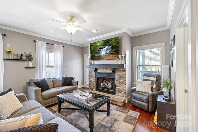 living room with crown molding, a stone fireplace, a ceiling fan, and wood finished floors