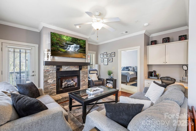 living room with a stone fireplace, visible vents, crown molding, and ceiling fan