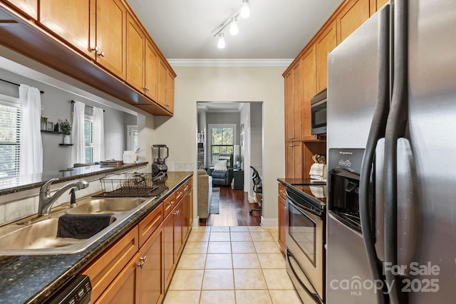 kitchen with brown cabinets, ornamental molding, light tile patterned floors, a sink, and appliances with stainless steel finishes
