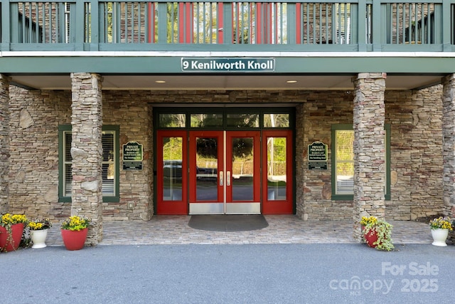 entrance to property featuring stone siding, a balcony, and french doors
