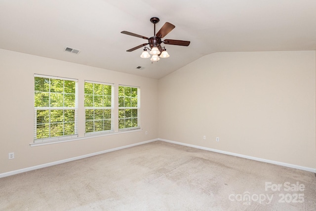 spare room featuring lofted ceiling, visible vents, a ceiling fan, baseboards, and light colored carpet