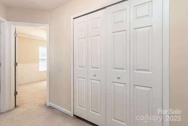 hall with light colored carpet, baseboards, ornamental molding, and a wainscoted wall