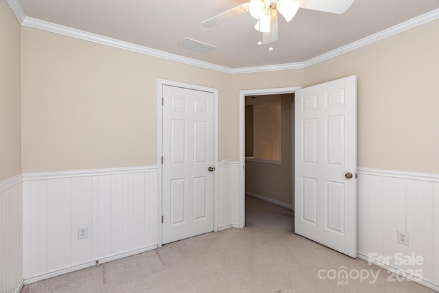 unfurnished bedroom featuring visible vents, a wainscoted wall, light colored carpet, and ornamental molding