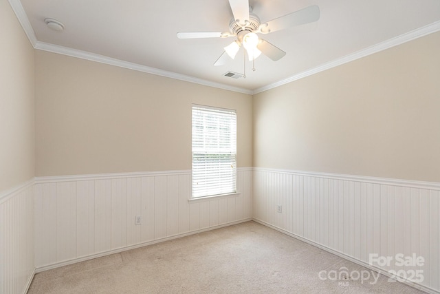 carpeted empty room with wainscoting, visible vents, and crown molding