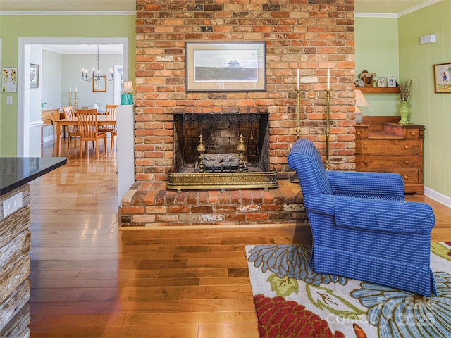 living room with ornamental molding, wood-type flooring, a chandelier, a brick fireplace, and baseboards