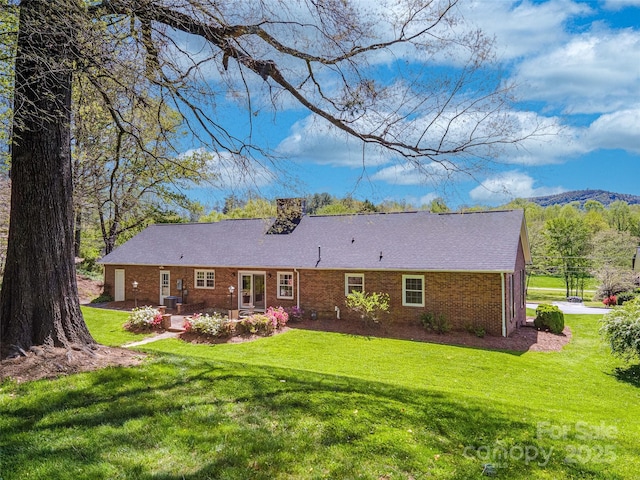 rear view of house featuring a yard, brick siding, a chimney, and a patio