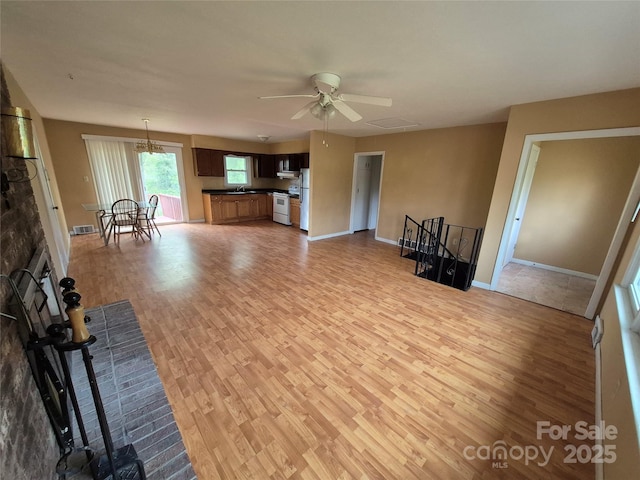unfurnished living room with baseboards, a ceiling fan, a sink, and light wood-style flooring