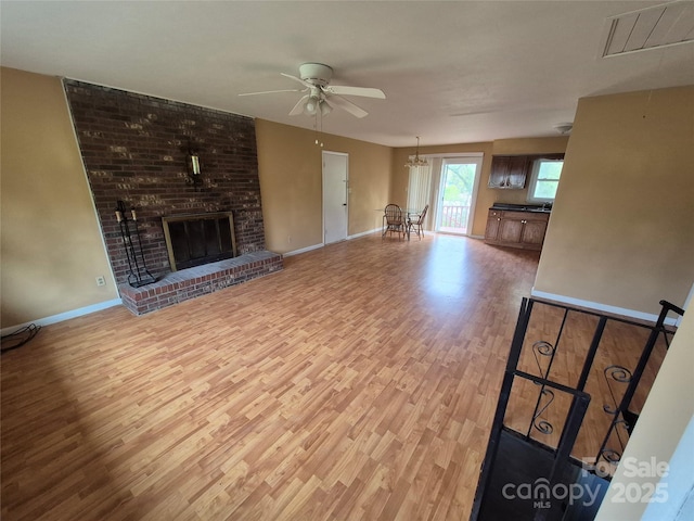 unfurnished living room with ceiling fan with notable chandelier, wood finished floors, baseboards, and visible vents
