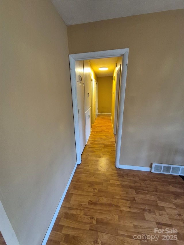 corridor with visible vents, light wood finished floors, and baseboards