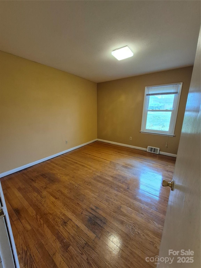 empty room with wood finished floors, visible vents, and baseboards