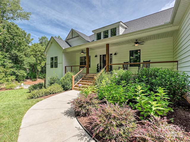view of front of property with a front yard, a ceiling fan, a shingled roof, and covered porch