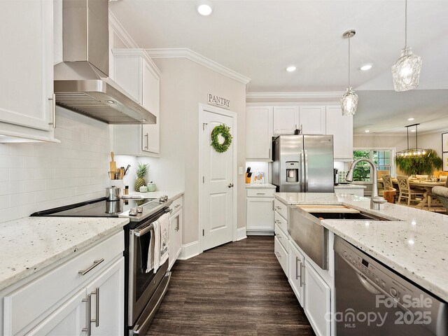kitchen featuring wall chimney exhaust hood, stainless steel appliances, white cabinetry, dark wood-type flooring, and hanging light fixtures