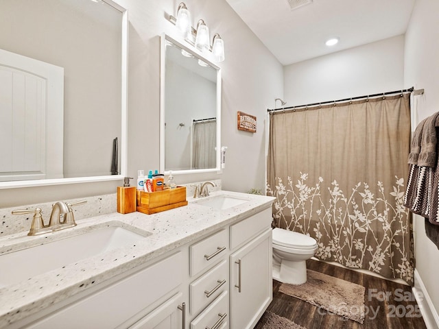 full bathroom featuring double vanity, wood finished floors, toilet, and a sink