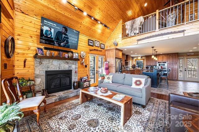 living area featuring wood finished floors, wood walls, a fireplace, track lighting, and high vaulted ceiling
