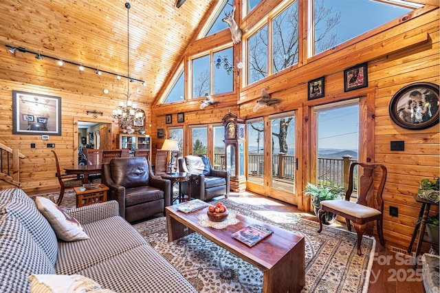 living area featuring high vaulted ceiling, wood walls, track lighting, and a chandelier