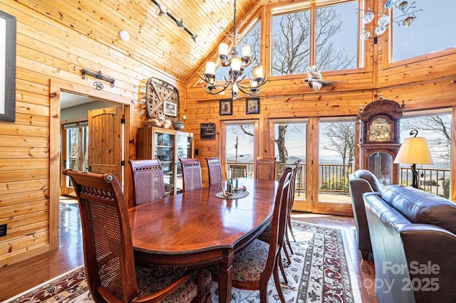 dining area with hardwood / wood-style floors, wooden walls, rail lighting, high vaulted ceiling, and a notable chandelier
