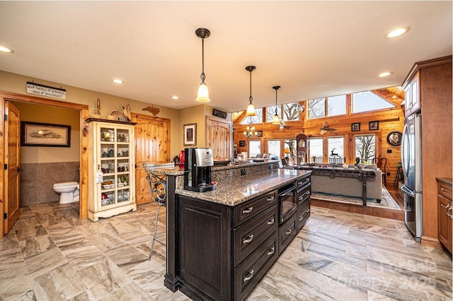 kitchen featuring freestanding refrigerator, a kitchen bar, wood walls, a kitchen island, and recessed lighting