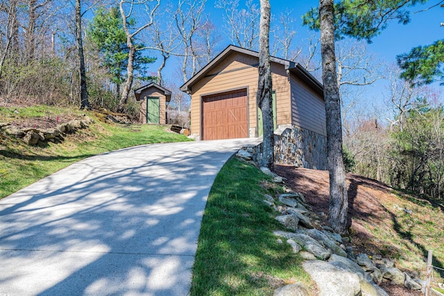 view of property exterior with stone siding, driveway, an outbuilding, and a garage