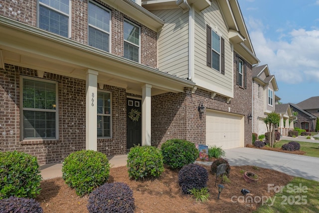 view of exterior entry featuring brick siding, a residential view, driveway, and a garage