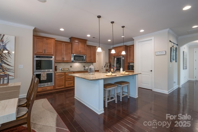 kitchen with arched walkways, dark wood finished floors, brown cabinetry, and stainless steel appliances