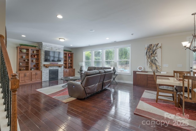 living room featuring crown molding, wood finished floors, stairs, a stone fireplace, and a chandelier