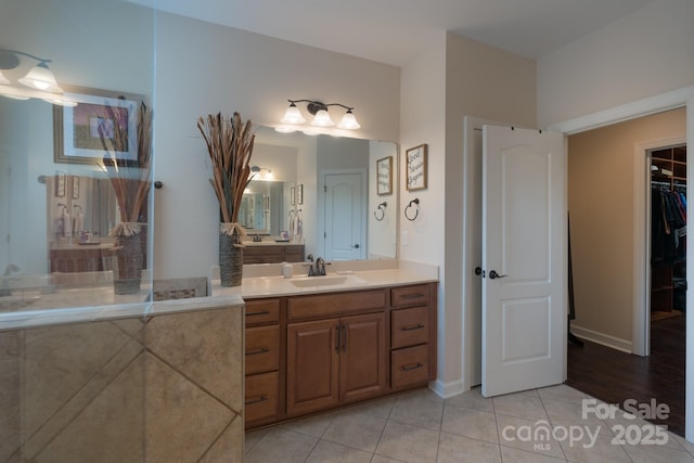 bathroom with a walk in closet, baseboards, vanity, and tile patterned floors