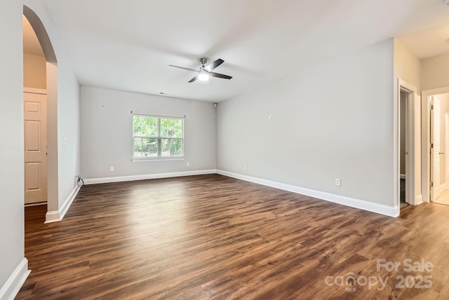 empty room with arched walkways, ceiling fan, dark wood-style flooring, and baseboards