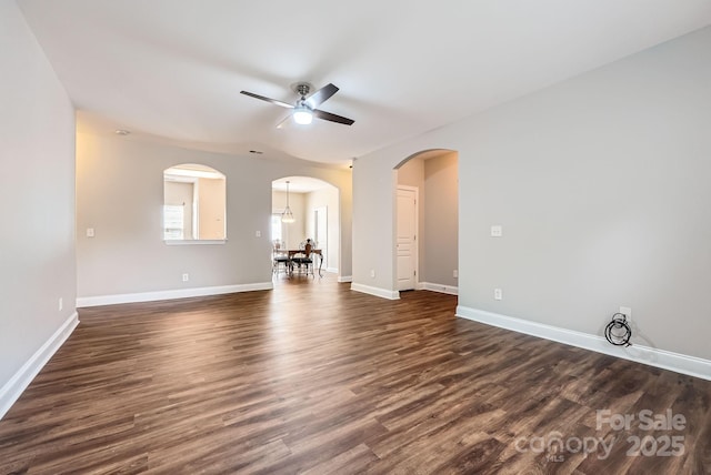 unfurnished room with arched walkways, a ceiling fan, baseboards, and dark wood-type flooring