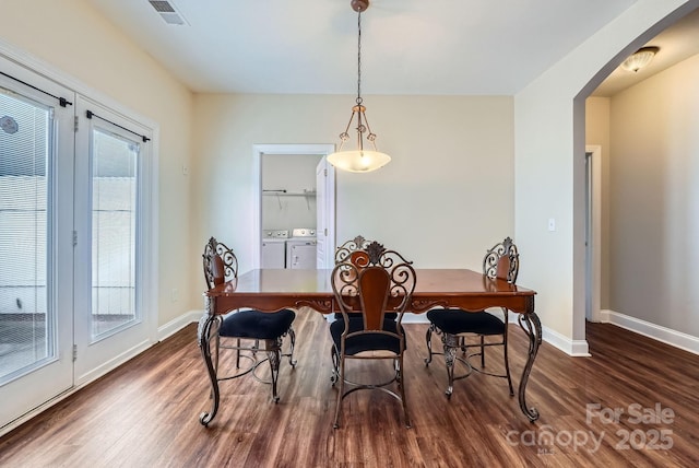 dining room featuring dark wood-type flooring, arched walkways, a wealth of natural light, and washer and clothes dryer