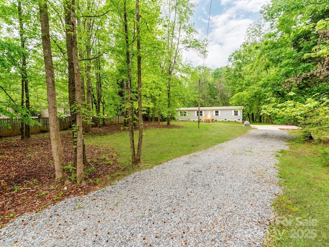 view of front of property featuring gravel driveway, fence, a wooded view, and a front yard