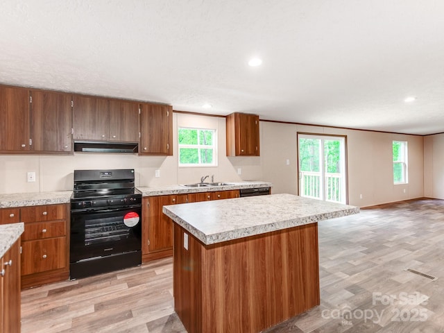 kitchen with brown cabinets, light wood finished floors, under cabinet range hood, a sink, and black gas stove