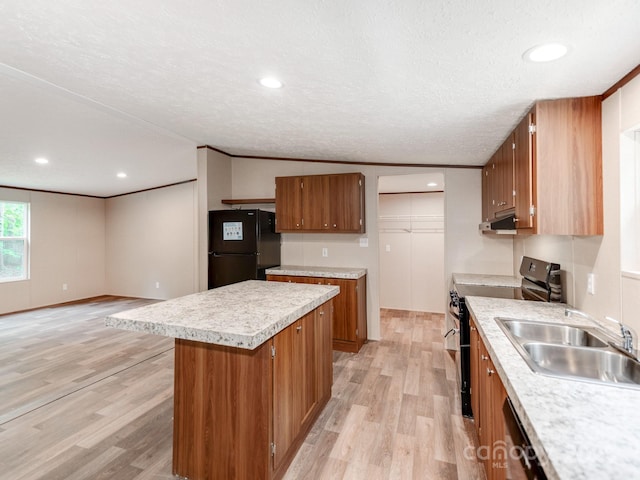 kitchen with a sink, brown cabinetry, stainless steel electric stove, under cabinet range hood, and freestanding refrigerator