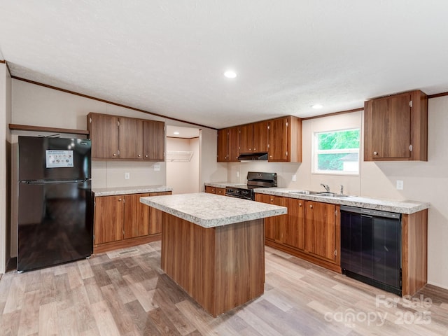 kitchen with under cabinet range hood, light countertops, a sink, light wood-type flooring, and black appliances