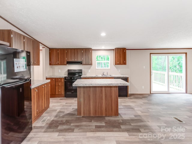 kitchen with a center island, brown cabinetry, black appliances, light countertops, and under cabinet range hood