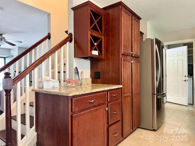 kitchen featuring a textured ceiling, freestanding refrigerator, ceiling fan, light stone countertops, and light tile patterned floors