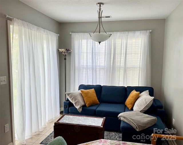 living area featuring a healthy amount of sunlight, a textured ceiling, visible vents, and light tile patterned floors