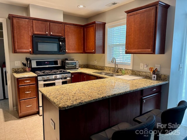 kitchen featuring a peninsula, a sink, visible vents, black microwave, and stainless steel gas stove