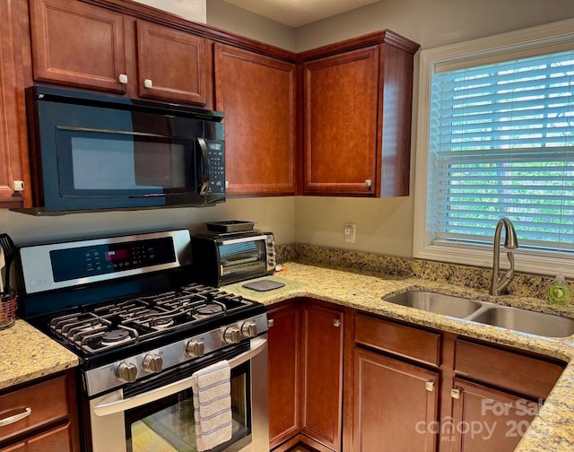 kitchen featuring a toaster, a sink, light stone countertops, black microwave, and stainless steel gas stove