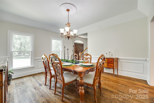 dining room featuring arched walkways, a wainscoted wall, a notable chandelier, a decorative wall, and light wood-style flooring