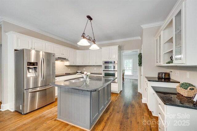 kitchen with white cabinets, a sink, dark stone countertops, stainless steel appliances, and ornamental molding