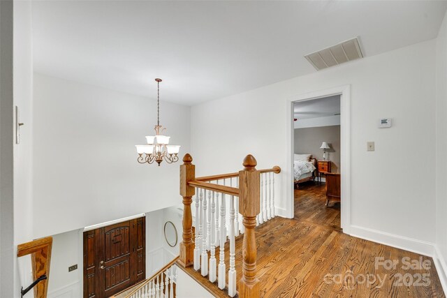 hall featuring a chandelier, baseboards, an upstairs landing, wood finished floors, and visible vents
