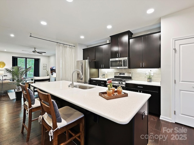 12641 Glowing Peak Rd, Huntersville, NC 28078 - kitchen with decorative backsplash, a kitchen island with sink, appliances with stainless steel finishes, light countertops, and a breakfast bar
