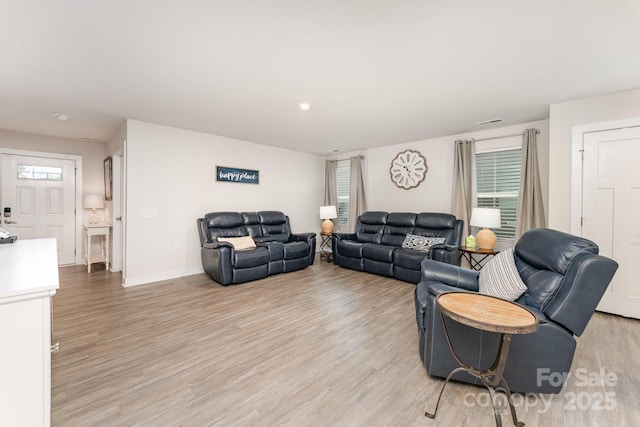 living area with baseboards, visible vents, light wood-style floors, and plenty of natural light
