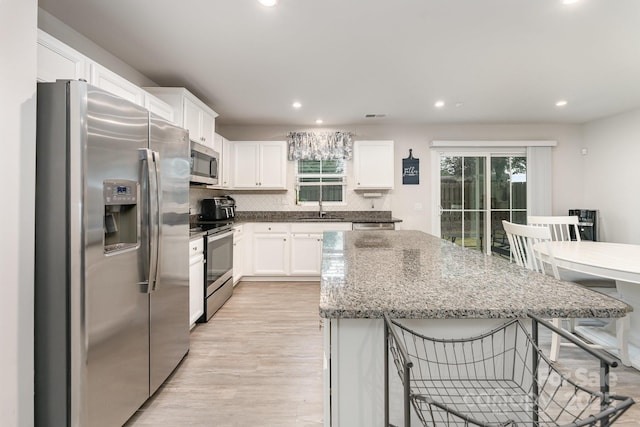 kitchen with a breakfast bar area, white cabinets, light wood-style flooring, appliances with stainless steel finishes, and a center island