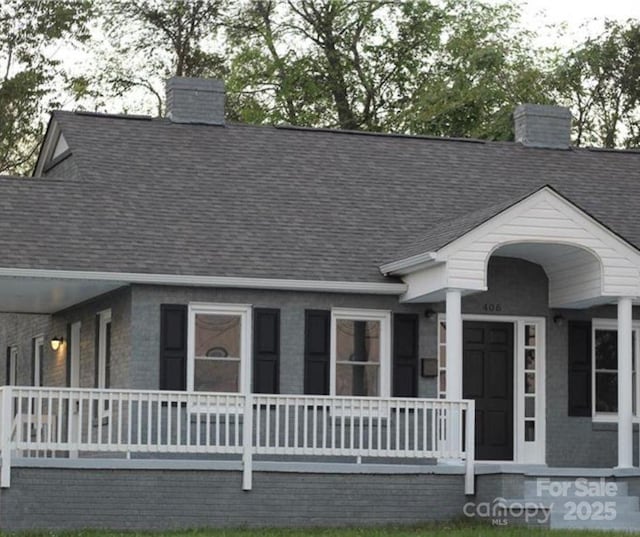 view of front of property with a shingled roof, a chimney, and covered porch