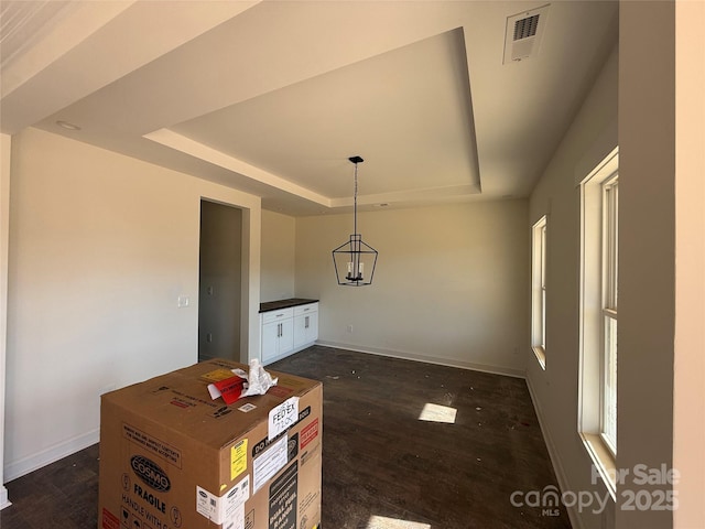 unfurnished dining area featuring a raised ceiling, visible vents, dark wood-type flooring, baseboards, and a notable chandelier