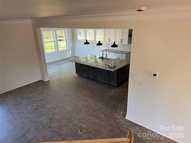 kitchen with dark wood finished floors, baseboards, light stone counters, an island with sink, and ornamental molding