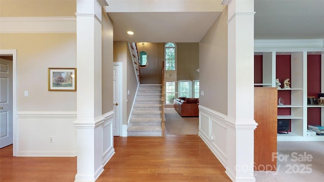 corridor featuring light wood-type flooring, decorative columns, and stairs