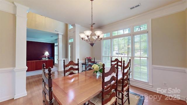 dining area with a chandelier, wood finished floors, visible vents, and ornate columns